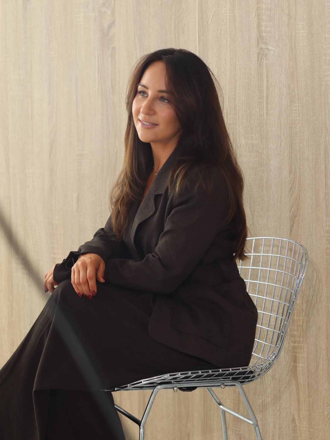 Melissa smiling, sitting on a wire chair